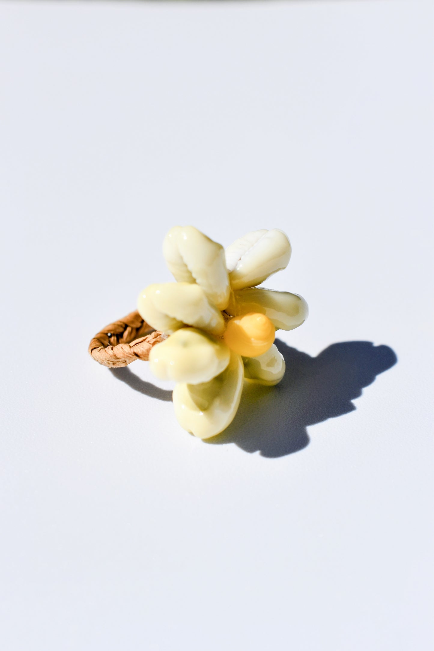 Bague en raphia tressé avec coquillages blanc naturel en forme de fleur, un savoir faire Polynésien, posé sur un fond blanc