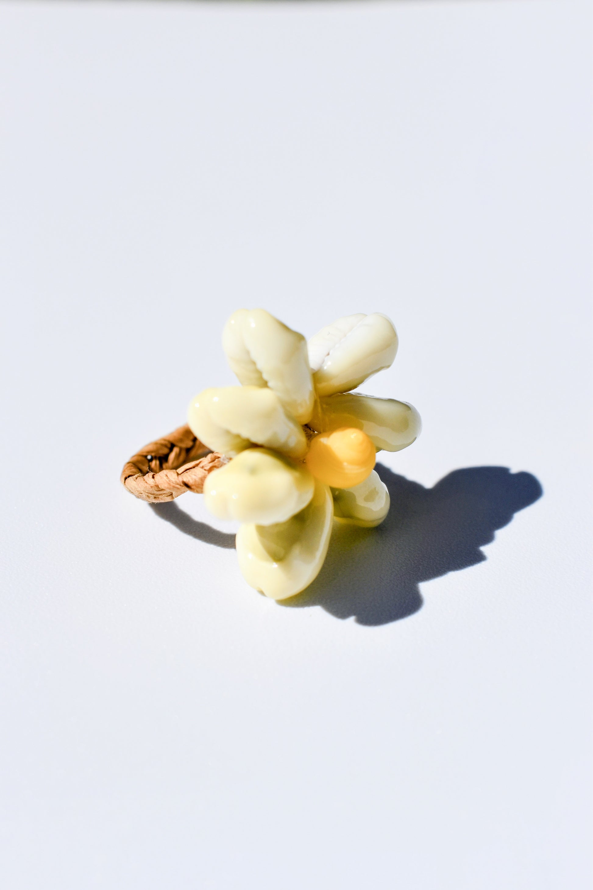 Bague en raphia tressé avec coquillages blanc naturel en forme de fleur, un savoir faire Polynésien, posé sur un fond blanc